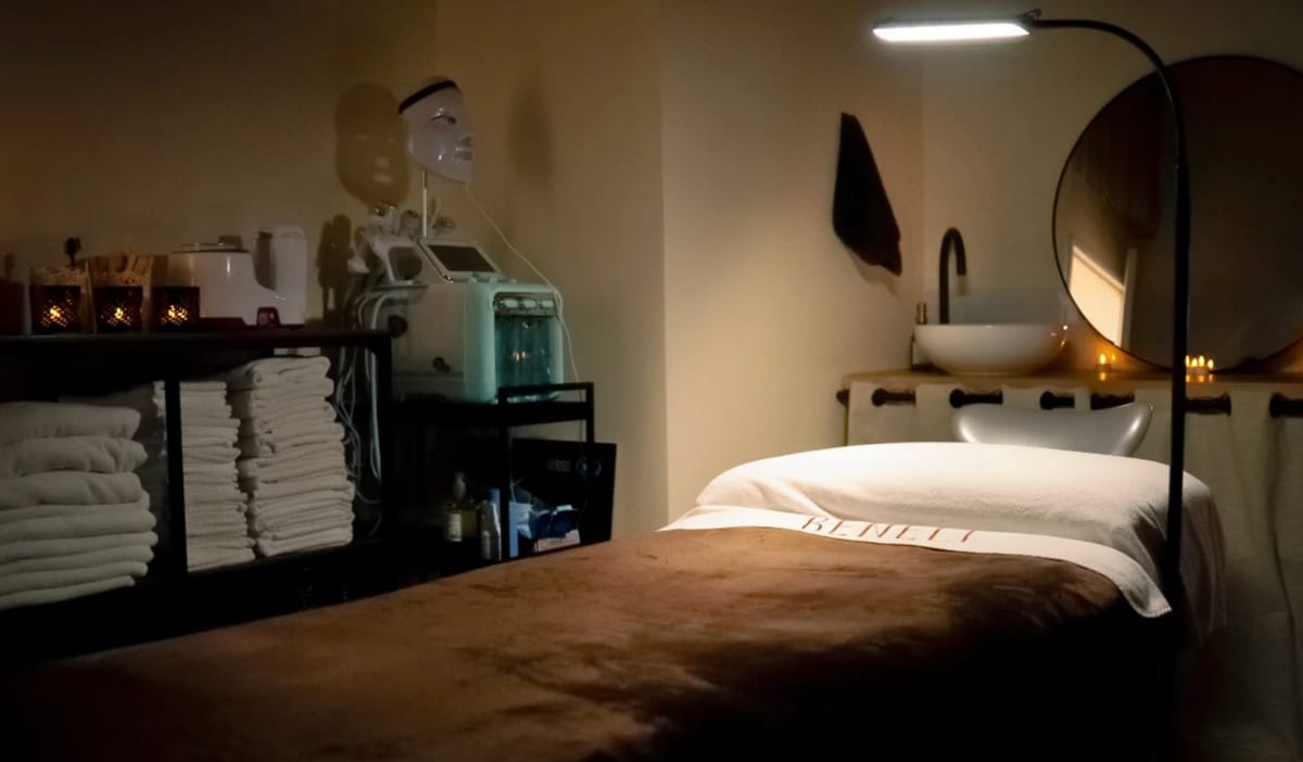 Une cabine de soin de Beneli Institut en lumière tamisée : table dressée avec le linge brodé Beneli, serviettes pliées et miroir rond